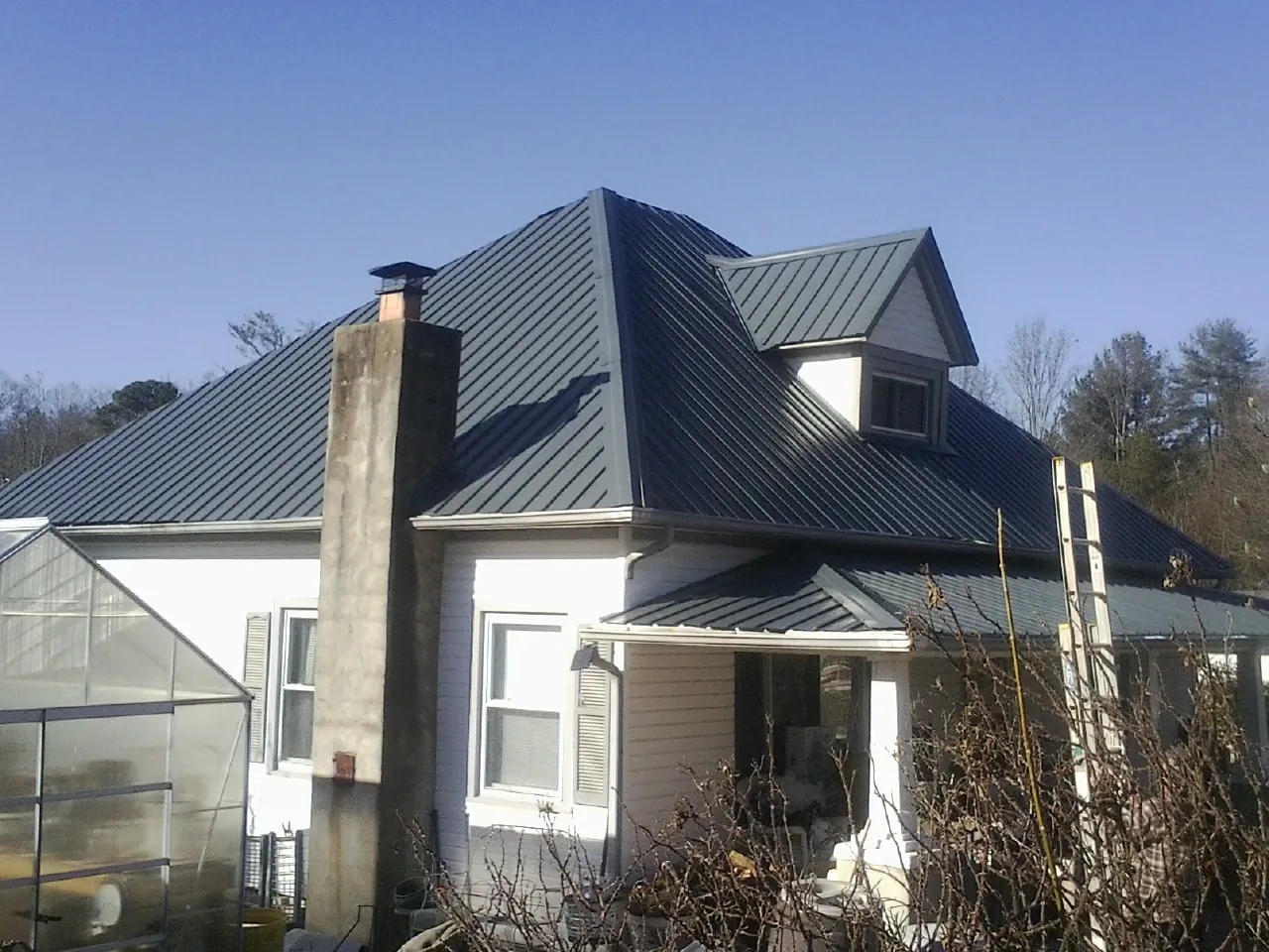 Dark blue standing seam metal roof on a white farmhouse with dormer — Slate & Tile Roof Repair by Roofing Brothers in Saraland