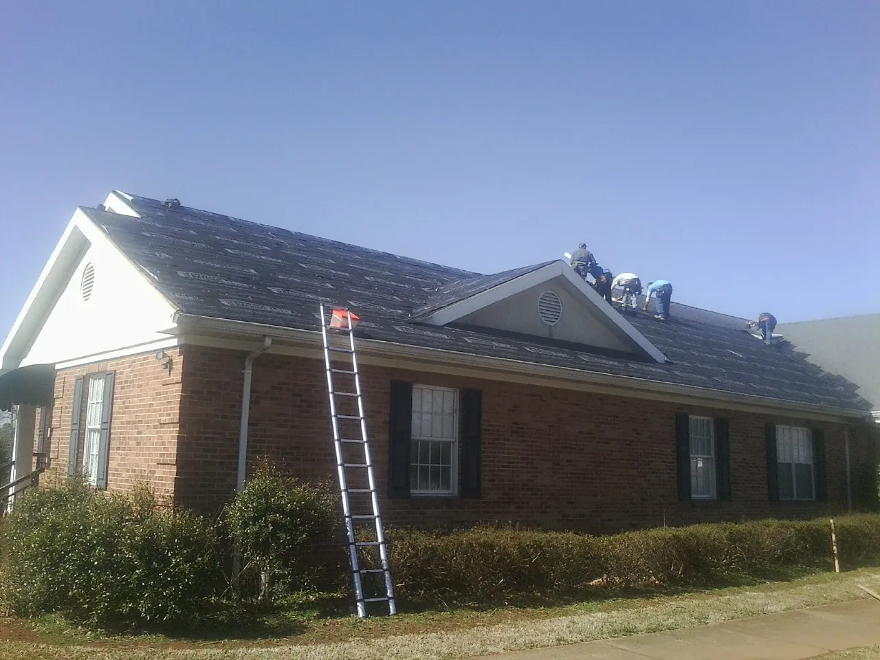 Crew tearing shingles off a brick ranch roof with a ladder set — Metal Roof Repair work by our crew in Saraland