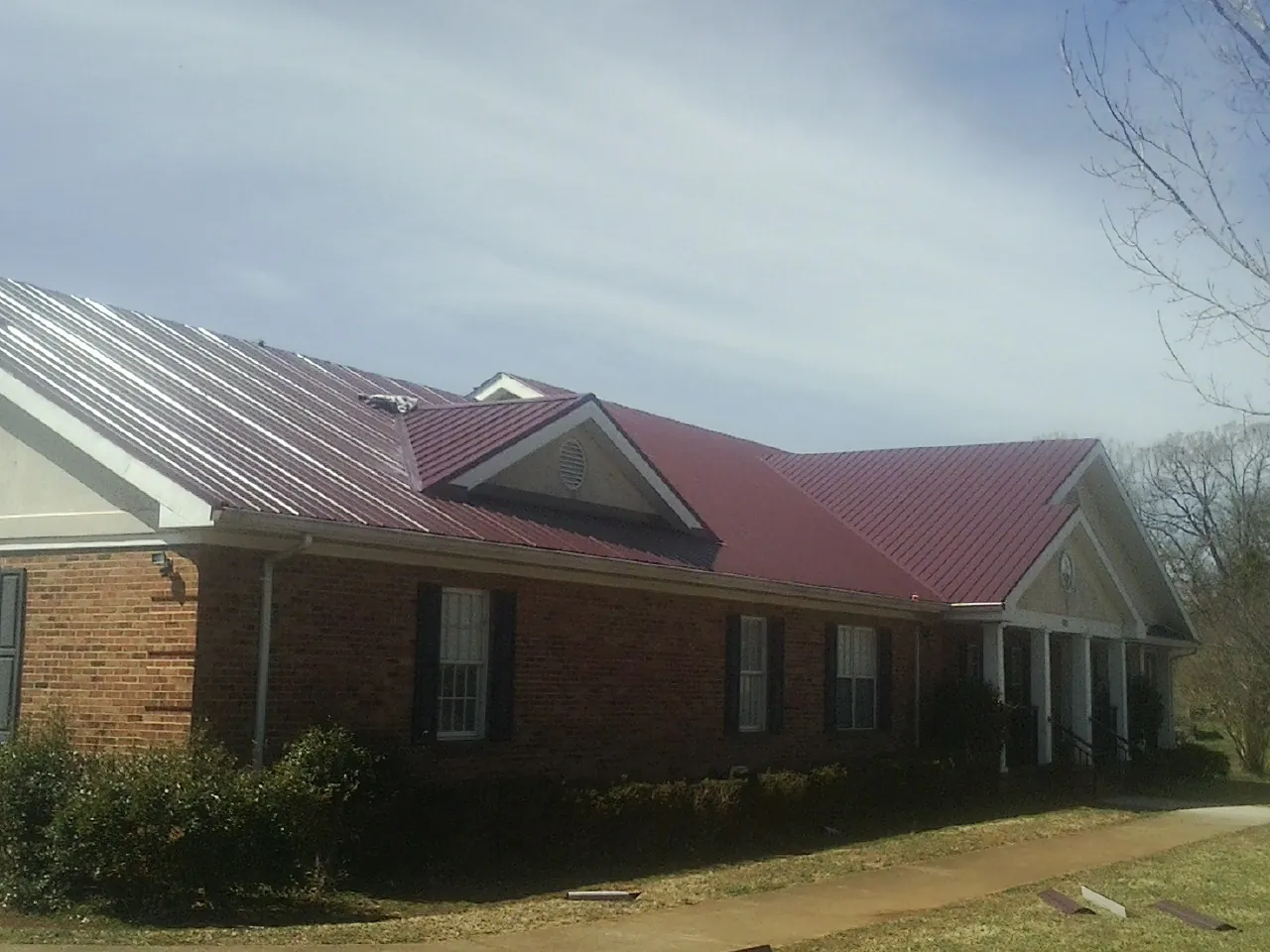 Red metal roof with gabled entries on a long brick building, from a Hail Damage Roof Repair job in Saraland