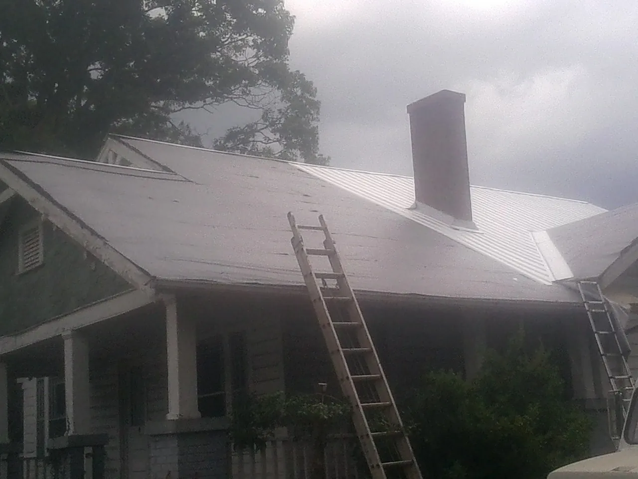 Ladders against a metal roof on an older home with a brick chimney in Saraland