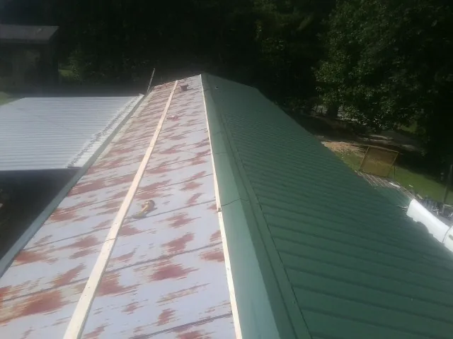 Old rusted panels beside newly installed green metal roofing — Wind Damage Roof Repair by Roofing Brothers in Saraland