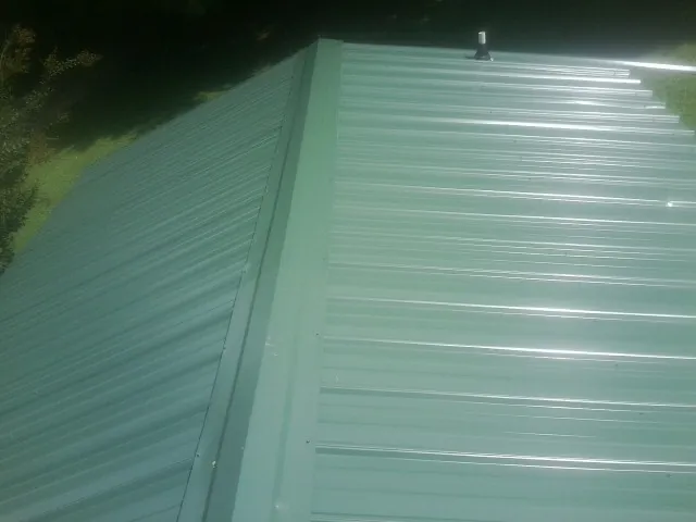 New green metal panels meeting at the ridge of a roof — Flat Roof Repair work by our crew in Saraland