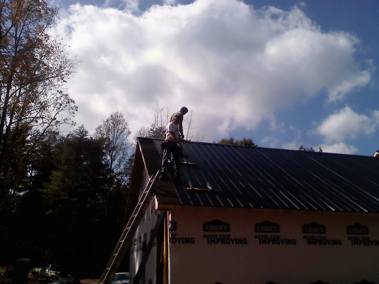 Roofer fastening dark metal panels high against a cloudy sky, from a Roof Inspection job in Saraland
