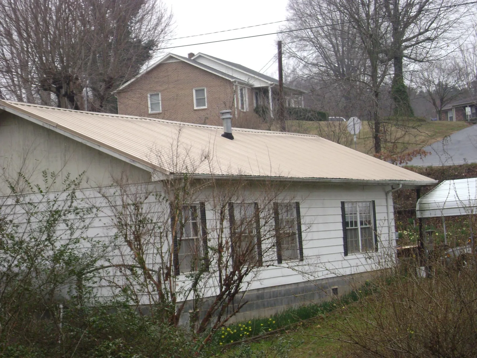 Tan metal roof on a white sided house set into a hillside — Commercial Roofing by Roofing Brothers in Saraland