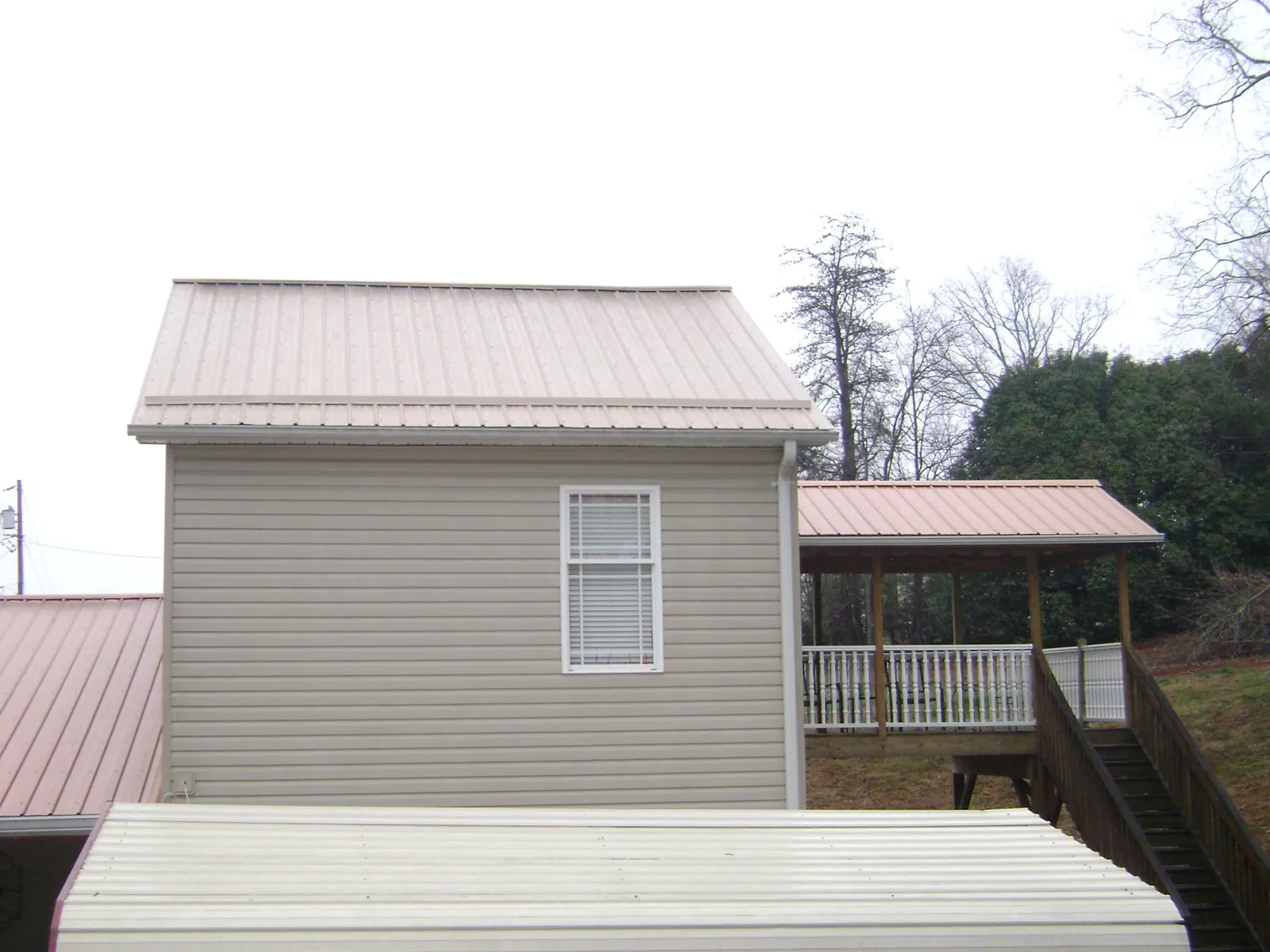 Tan metal roofs on a two story addition and attached porch, from a Roof Replacement job in Saraland